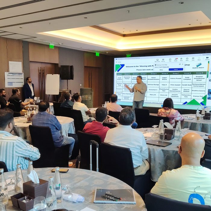 Best Software Sales Training Company for Sales Growth A corporate sales trainer delivering an IT industry sales strategy presentation to technology professionals seated at round banquet tables in a conference hall.
